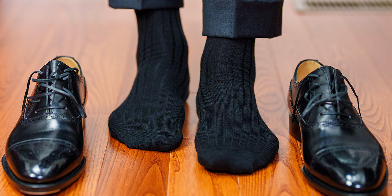 man wearing black church socks standing on hardwood floor with black oxfords beside his feet
