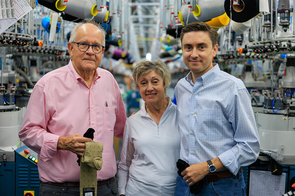 The James family of Boardroom Socks smiling and standing together in front of sock knitting machines.