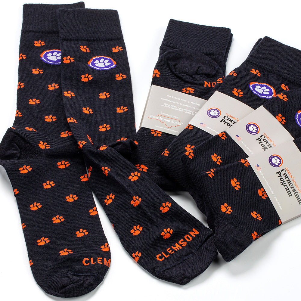 Dark navy dress socks decorated with Clemson tiger paw prints and CLEMSON stitched across the toe. Several socks are wrapped in Clemson branded packaging, all on a white background.
