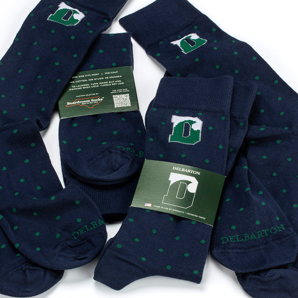 Four pairs of navy dress socks with green polka dots and a green Delbarton logo, shown with their green paper packaging bands on a white background.
