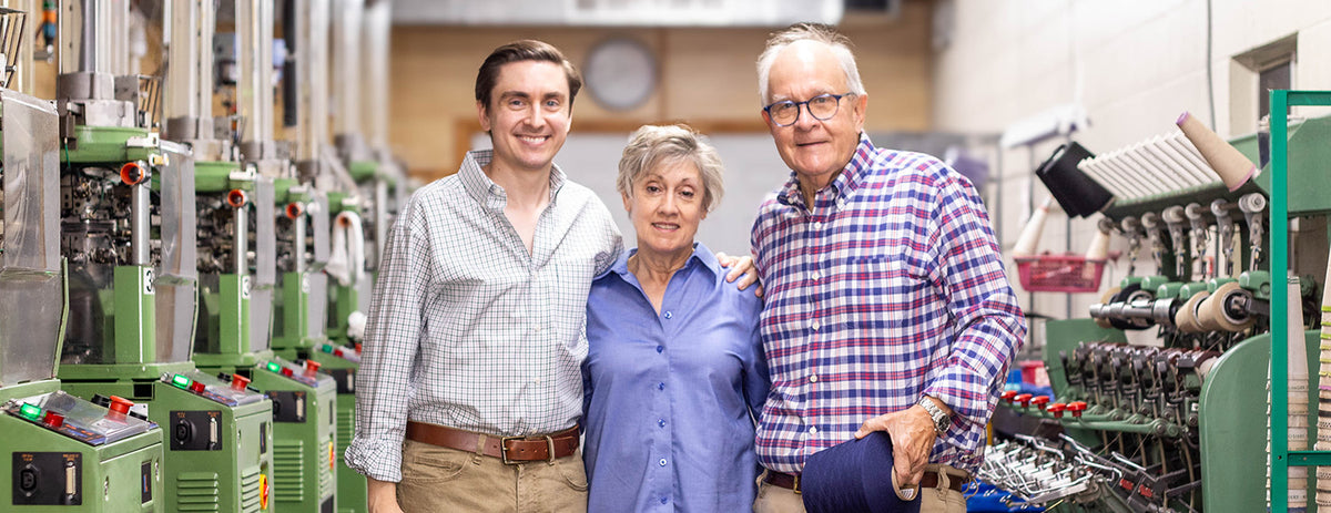 James family of Boardroom Socks smiling and standing together in front of knitting machines.