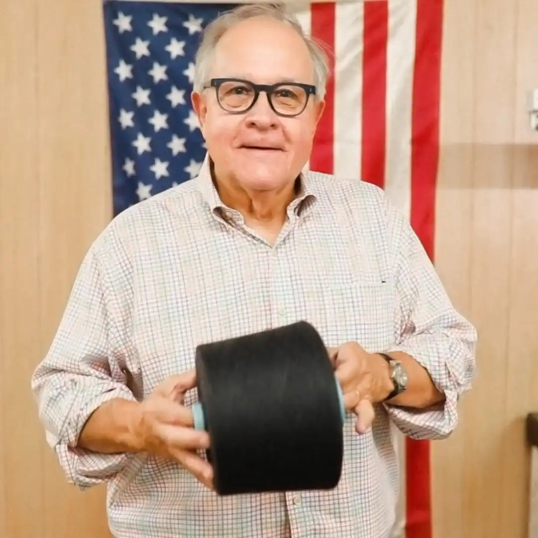 Mike James from Boardroom Socks holding cone of yarn while standing in front of American flag