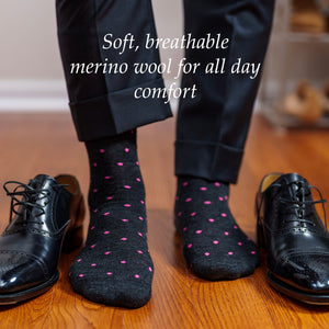 man wearing charcoal grey dress socks with pink dots while standing on hardwood floor beside black oxfords