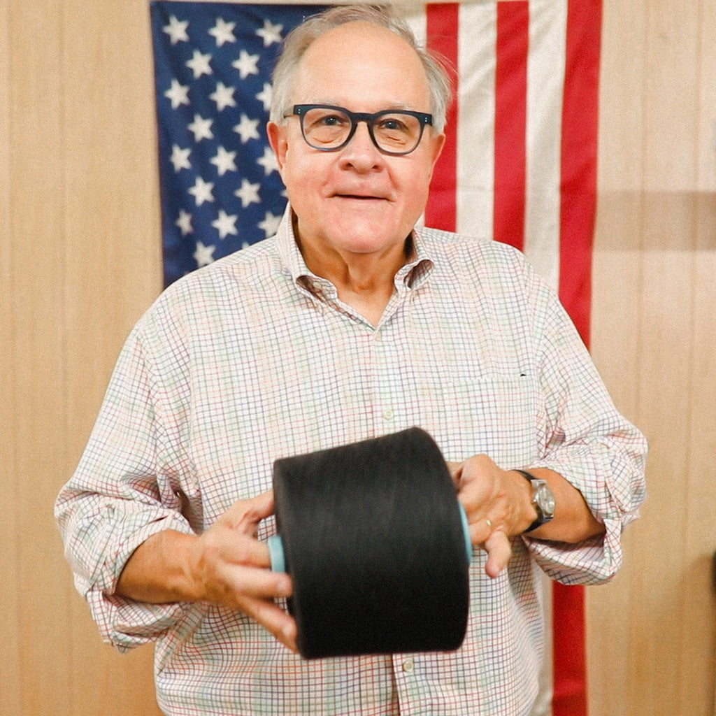 Mike from Boardroom Socks holding cone of yarn standing in front of American flag