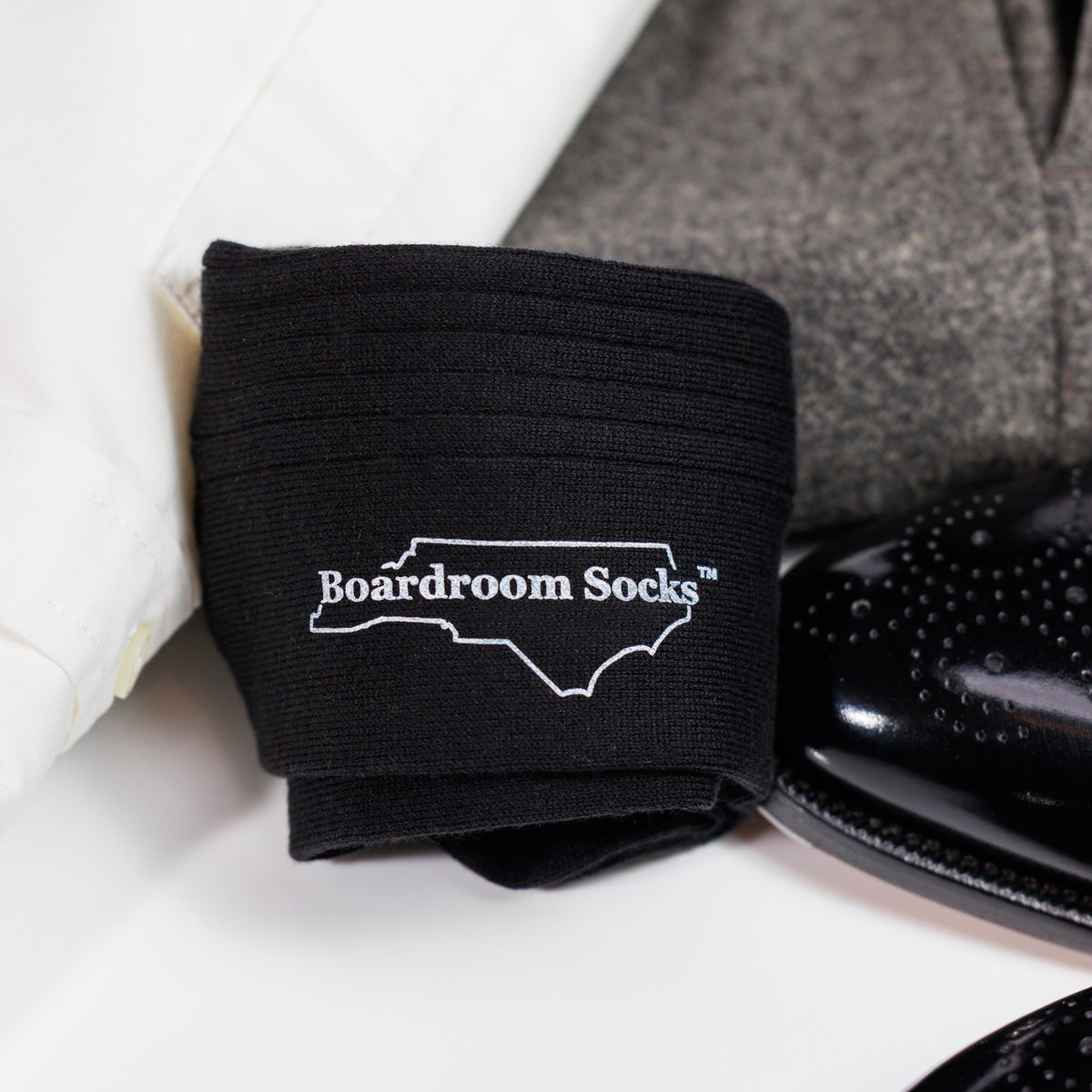 Black Cotton Mid Calf Dress Socks rolled up resting on dress clothes and shoes