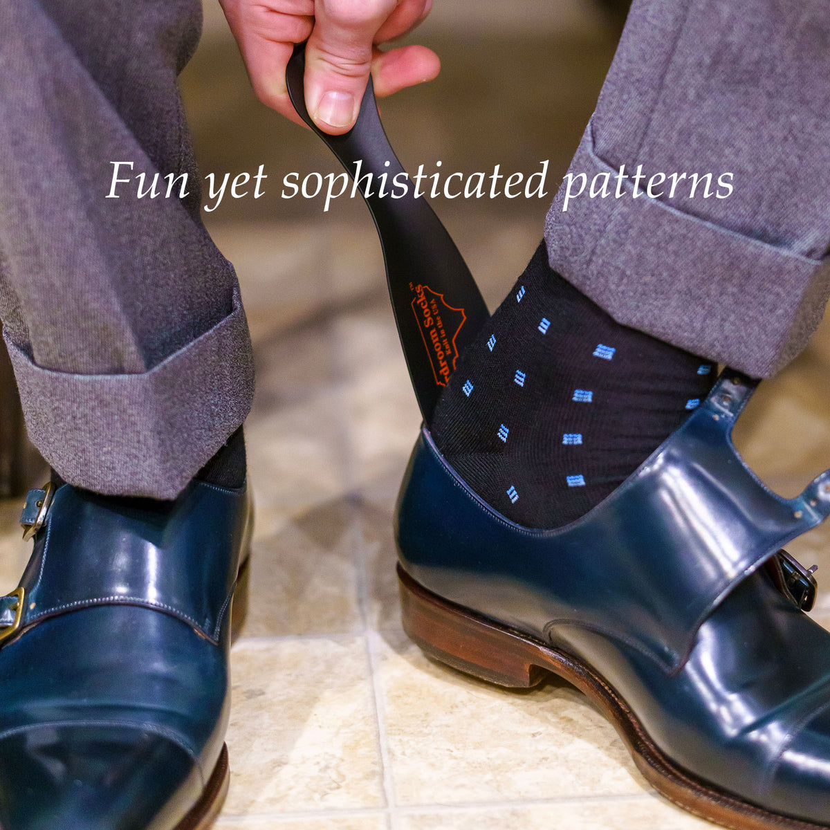 man using shoe horn to slide black and blue patterned dress socks into navy monkstrap dress shoes