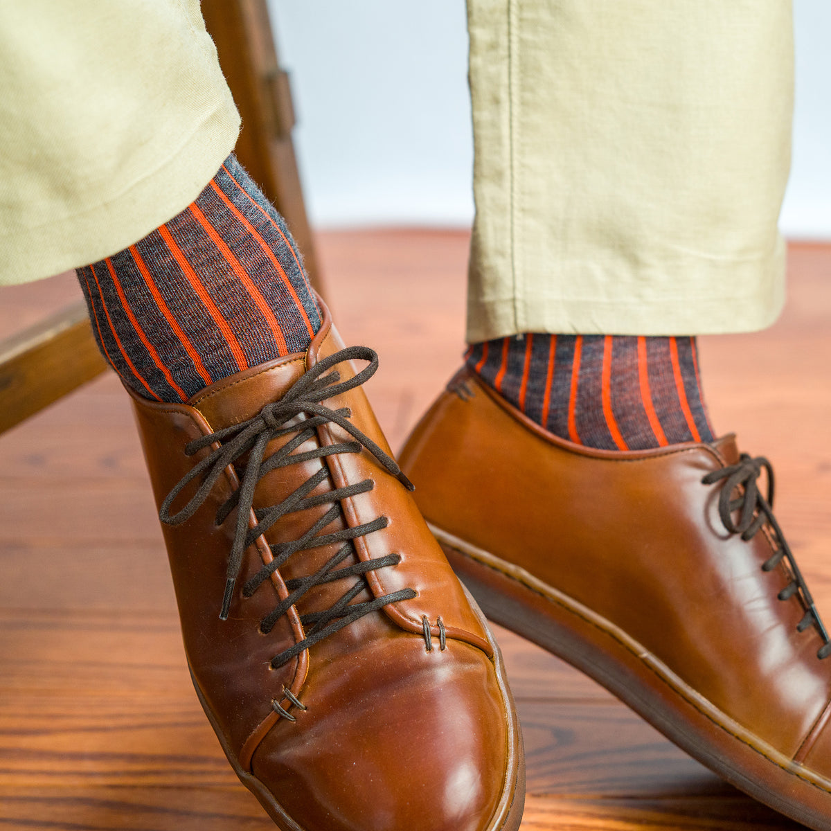 man seated on stool wearing grey and orange shadow stripe dress socks with chinos with brown leather sneakers