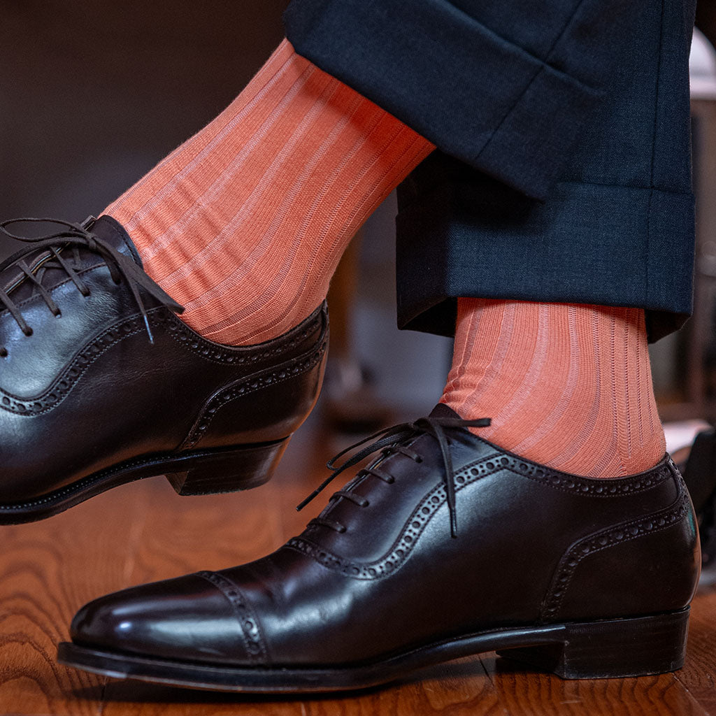 man crossing ankles wearing peach colored cotton dress socks with charcoal grey suit and dark brown oxfords