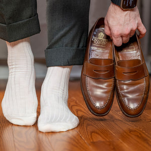 man wearing natural wool dress socks holding brown penny loafers in hand