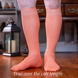 man wearing peach over the calf dress socks standing on hardwood floor