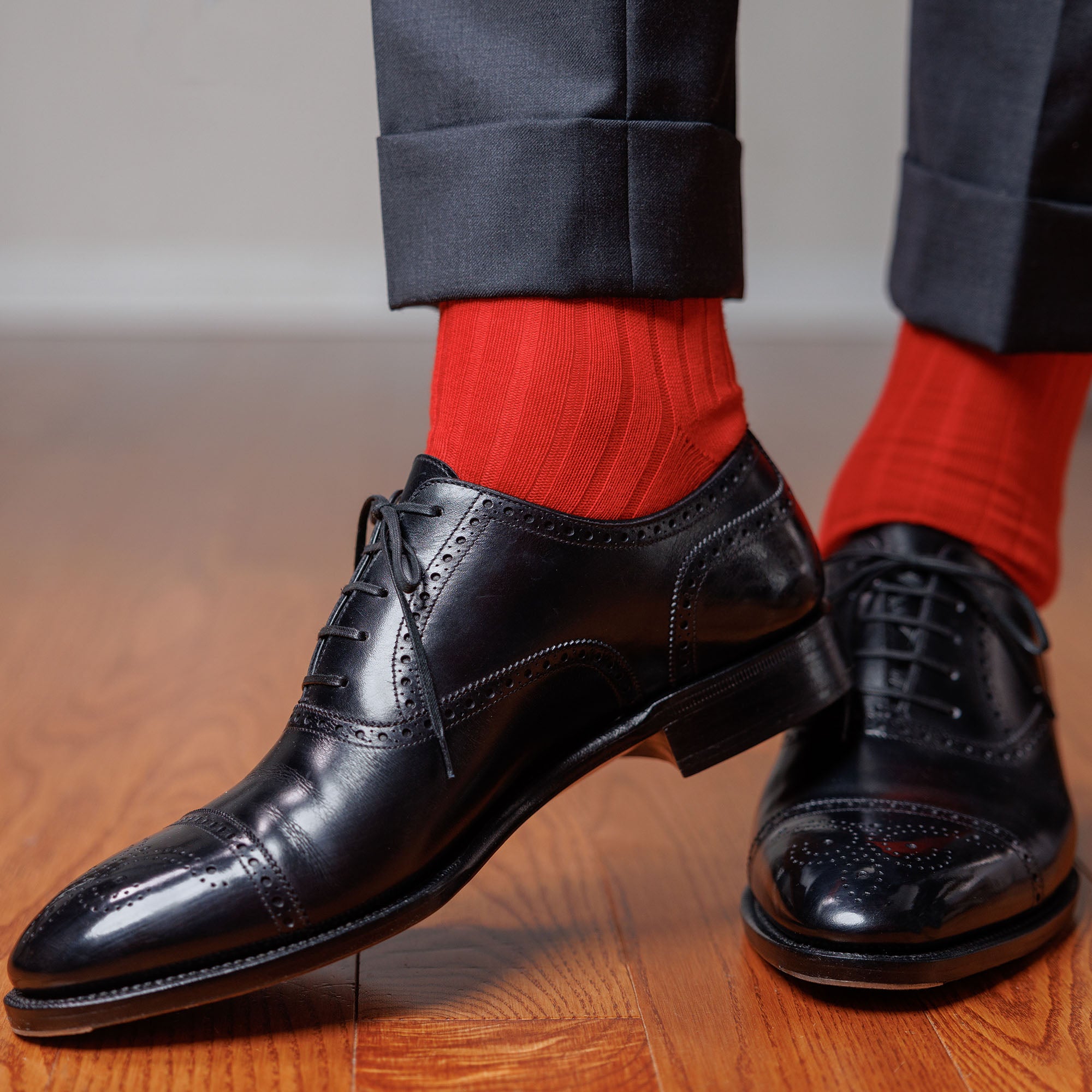 man wearing bright red dress socks with black oxfords and charcoal slacks standing on hardwood floor