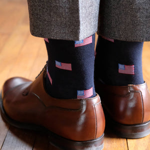 man standing on hardwood floor wearing American flag dress socks and brown oxfords with light grey trousers