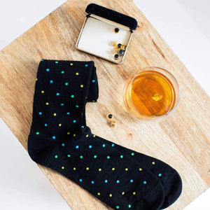 Pair of Black Patterned Dress Socks Sitting on a Stool with Cuff Links and a Glass of Bourbon