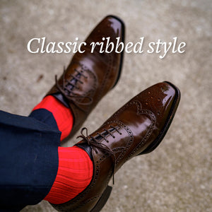 man crossing ankles wearing bright red dress socks with navy dress pants and brown brogue wingtips