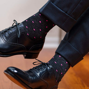 man crossing legs wearing grey dress socks with bright pink dots and charcoal trousers with black oxfords
