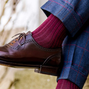 man crossing legs wearing burgundy merino wool dress socks with plaid dress pants and brown dress shoes