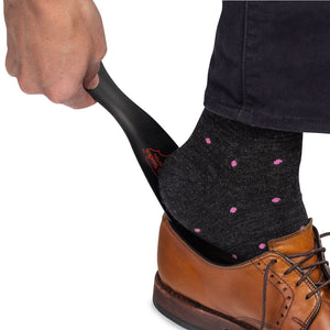 man using black shoe horn to put on brown leather dress shoes