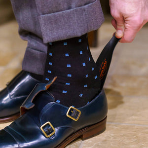 man wearing black and blue patterned dress socks using a shoe horn to put on dark blue dress shoes