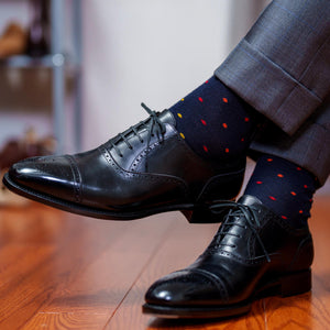 man crossing ankles wearing navy dress socks decorated with colorful polka dots