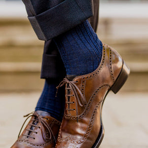 man crossing ankles wearing navy wool dress socks and light brown oxford dress shoes