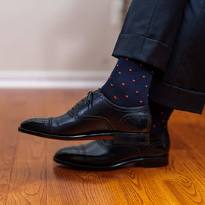 man crossing legs wearing navy and orange patterned dress socks with black oxfords and dark grey trousers