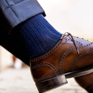 man crossing legs wearing navy merino wool dress socks and brown dress shoes