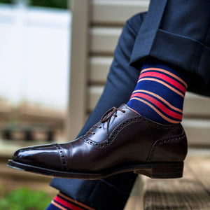 man crossing legs wearing colorful striped dress socks with navy trousers and dark brown oxfords