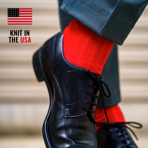 man standing wearing bright red merino wool dress socks and navy pants with black dress shoes while crossing ankles