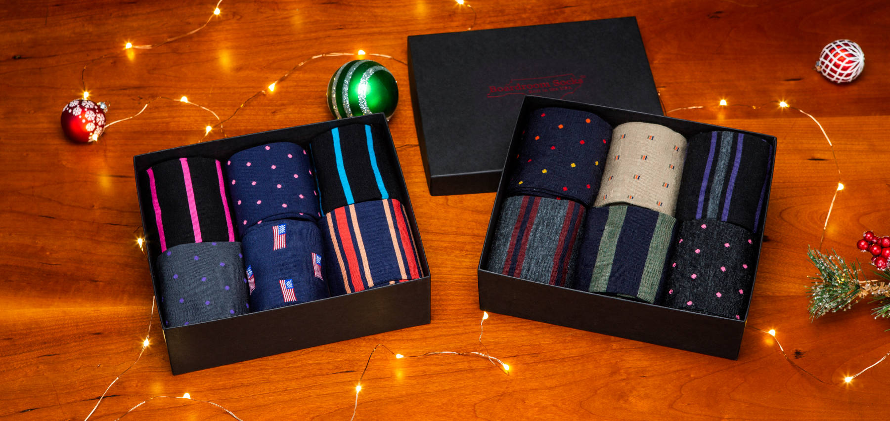 two gift boxes filled with colorful dress socks arranged on a wooden table with holiday decor