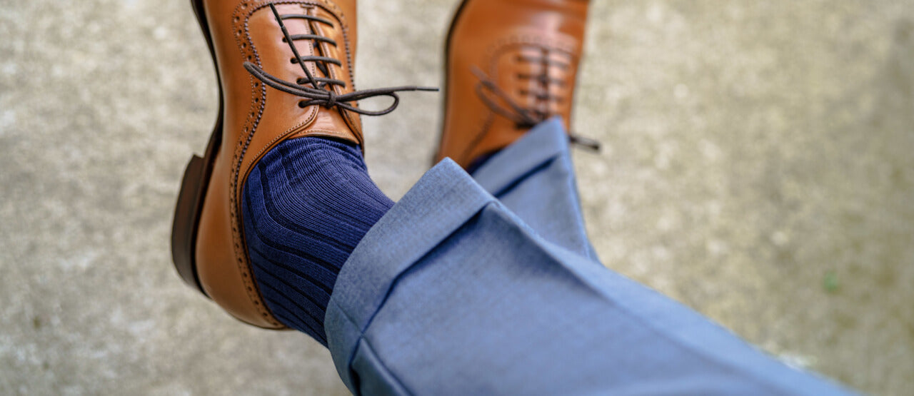 man crossing legs wearing baby blue dress pants with navy blue dress socks and brown shoes