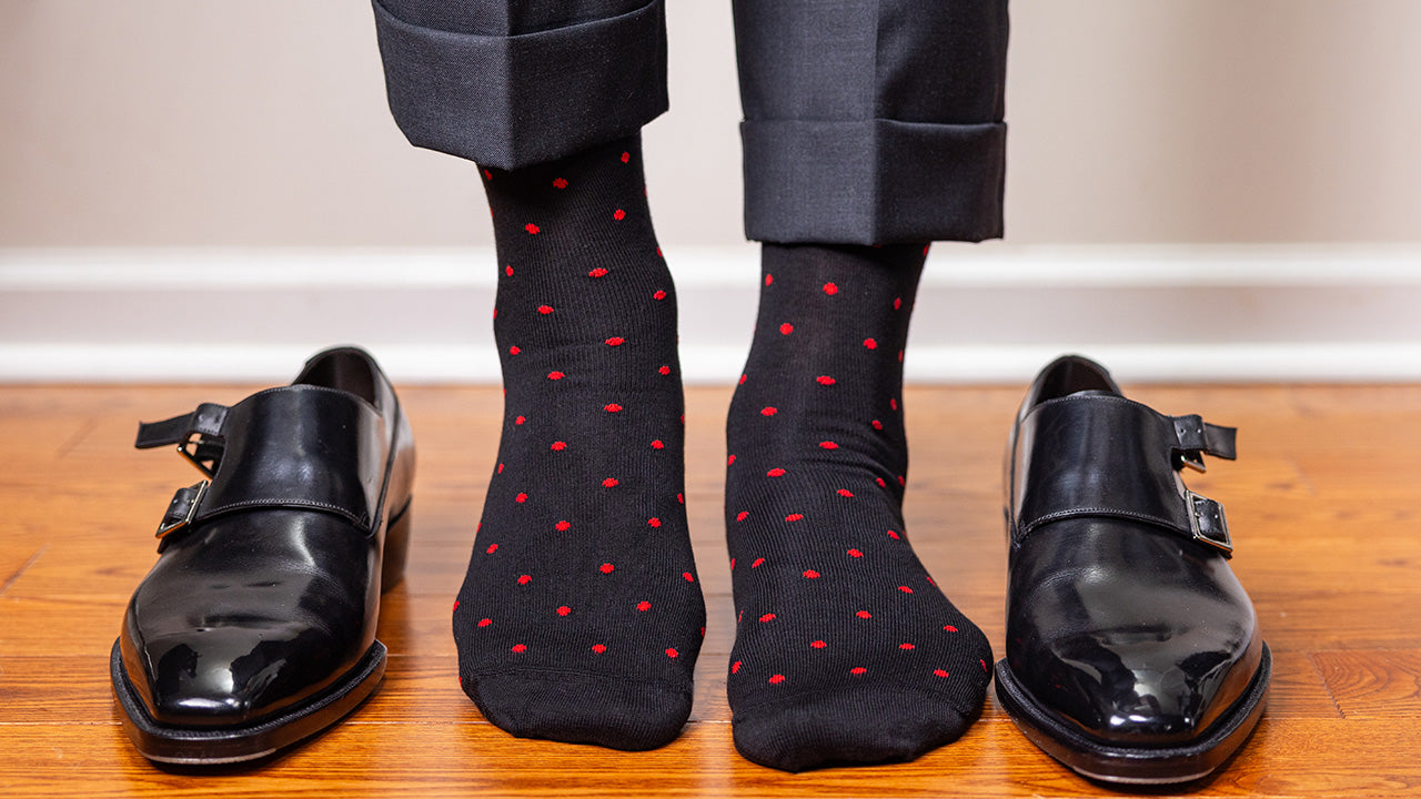 man standing on hardwood floor wearing black cotton dress socks decorated with small red polka dots