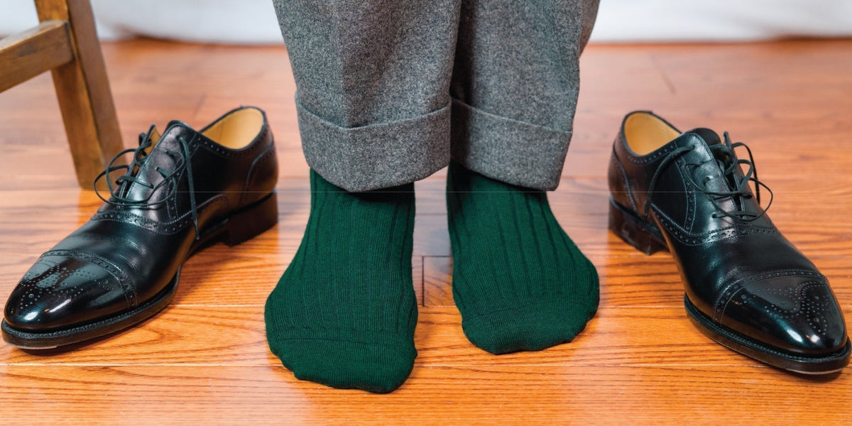 Man standing on hardwoodfloors wearing forest green merino wool dress socks and grey pants