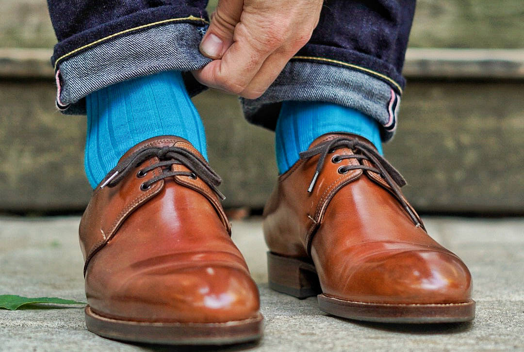 man wearing bright teal colorful dress socks adjusting pants