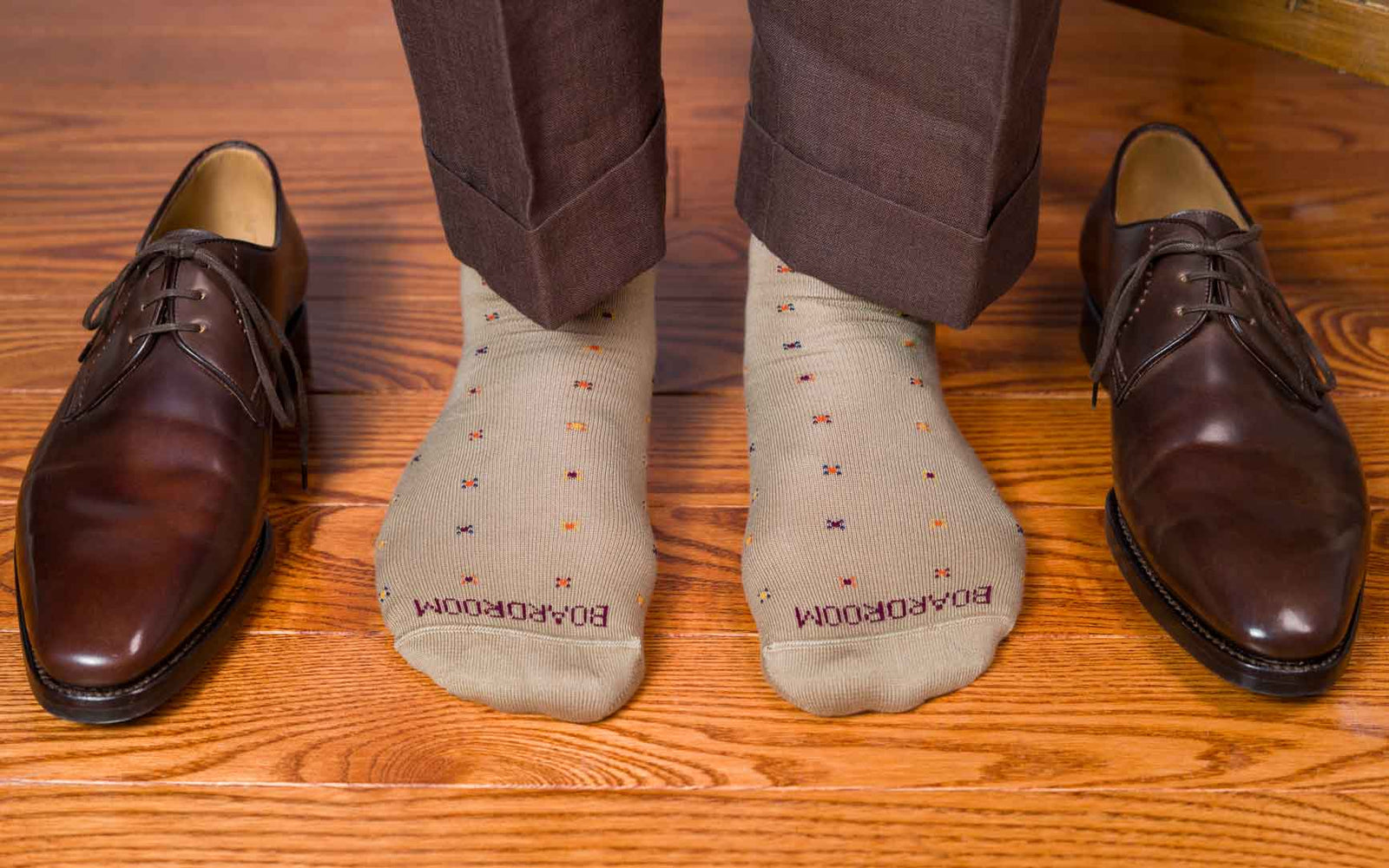 man standing on wood floor wearing khaki dress socks with geometric pattern