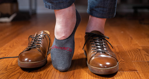 man putting on brown leather dress sneakers with grey no show dress socks