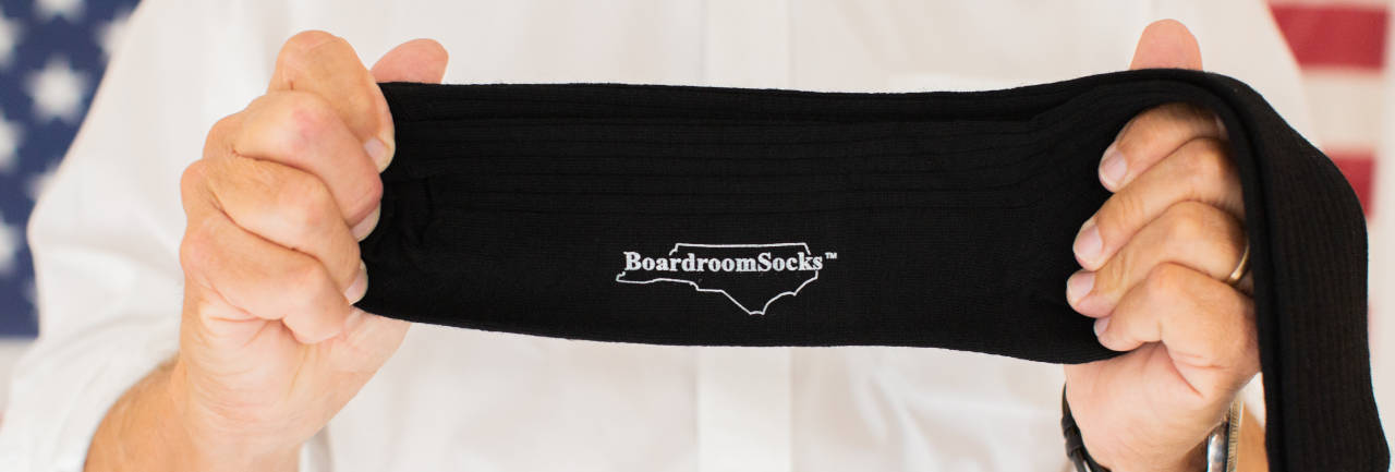 man holding thin black dress socks while standing in front of American flag