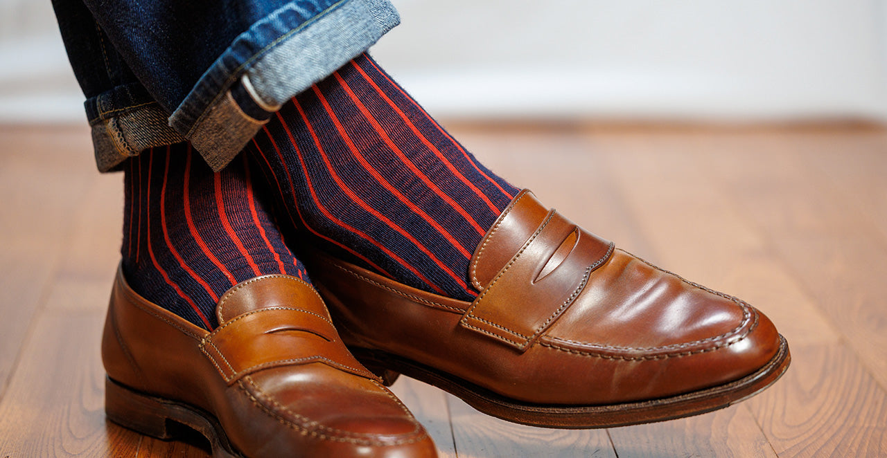 man wearing navy and red vertical ribbed shadow stripe dress socks with brown penny loafers and jeans