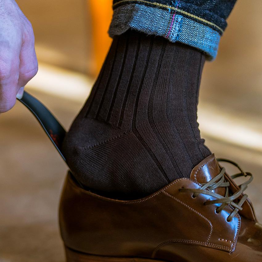 man wearing brown cotton dress socks putting on shoe with a shoe horn