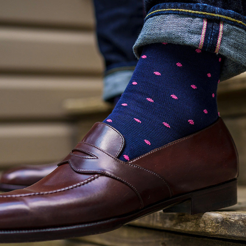 man wearing navy and pink patterned dress socks with jeans and shined penny loafers with foot on step