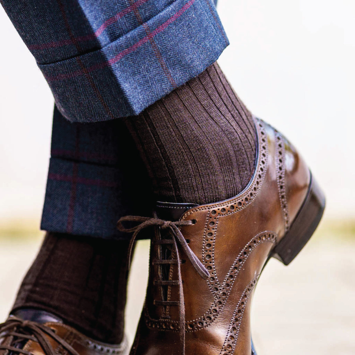 close up of a man crossing legs wearing plaid pants and brown merino wool ribbed dress socks 