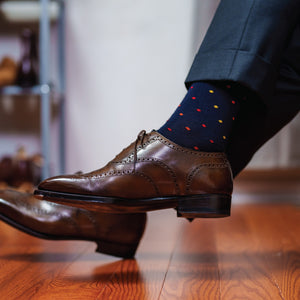 man crossing legs wearing navy merino wool dress socks with multi colored polka dots