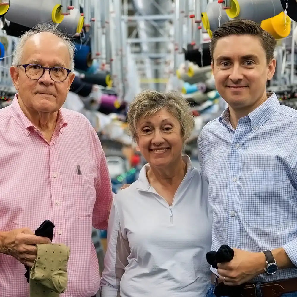 three members of James family from Boardroom Socks smiling and standing together in hosiery mill
