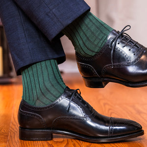 man crossing legs wearing British racing green dress socks with navy trousers and black oxfords