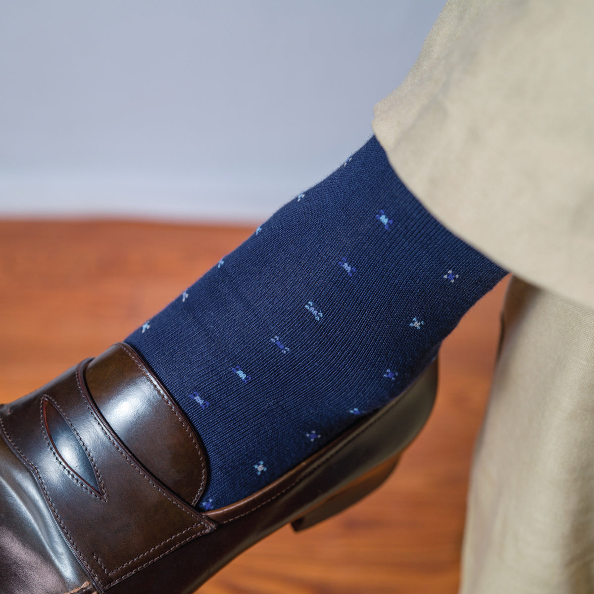 man crossing legs wearing khakis and navy mid calf cotton geometric pattern socks