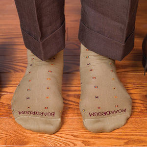 man standing on a wood floor wearing mid calf length khaki geometric pattern dress socks and brown slacks
