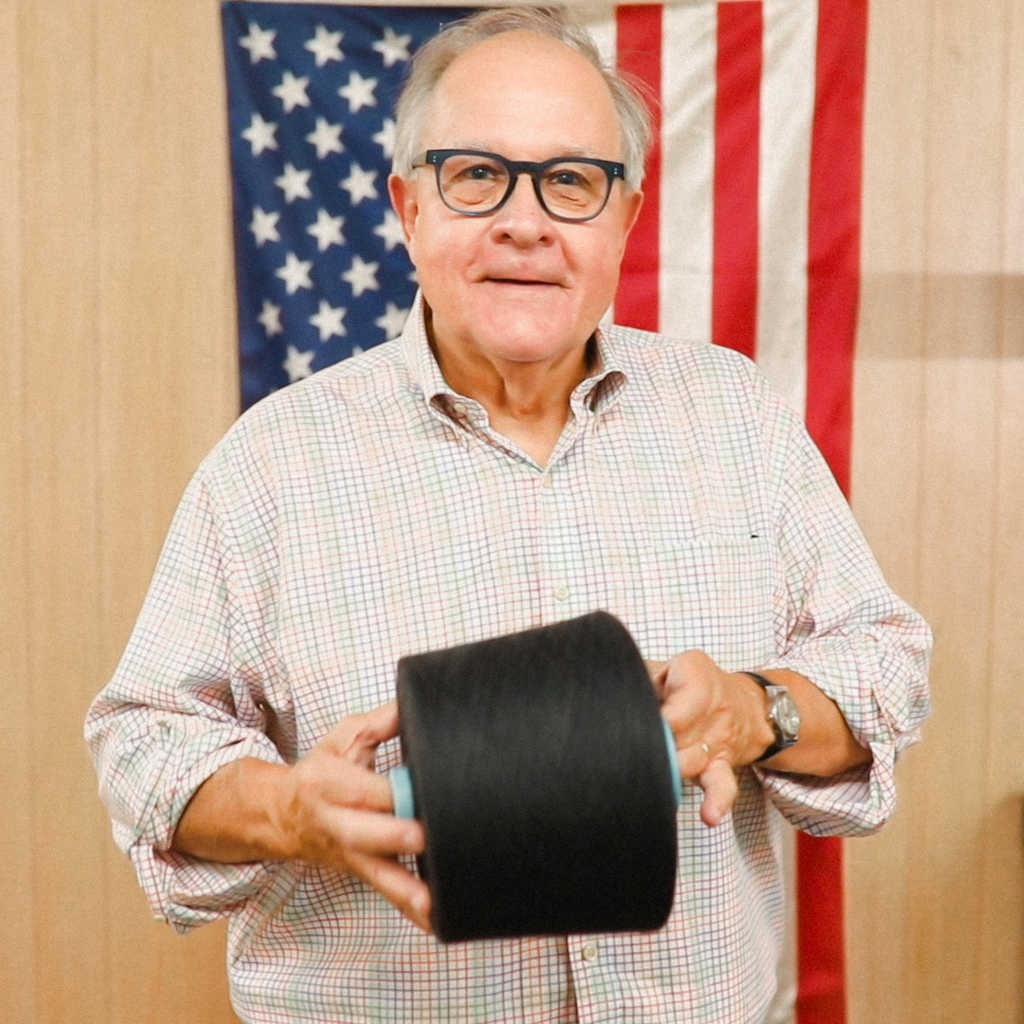 Mike James holding cone of merino wool yarn in front of American flag