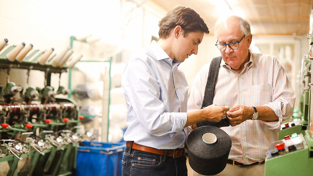 Nathan and Mike James of Boardroom Socks standing in front of knitting machine examining socks and yarn.