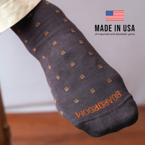 detailed image of brown patterned dress sock on foot worn with American flag image and text overlay about being made in the USA of imported and domestic yarns
