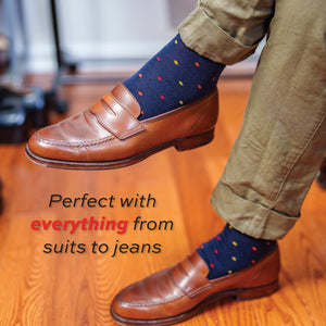 man crossing his legs wearing brown loafers and navy over the calf merino wool dress socks in a tri-color dot pattern