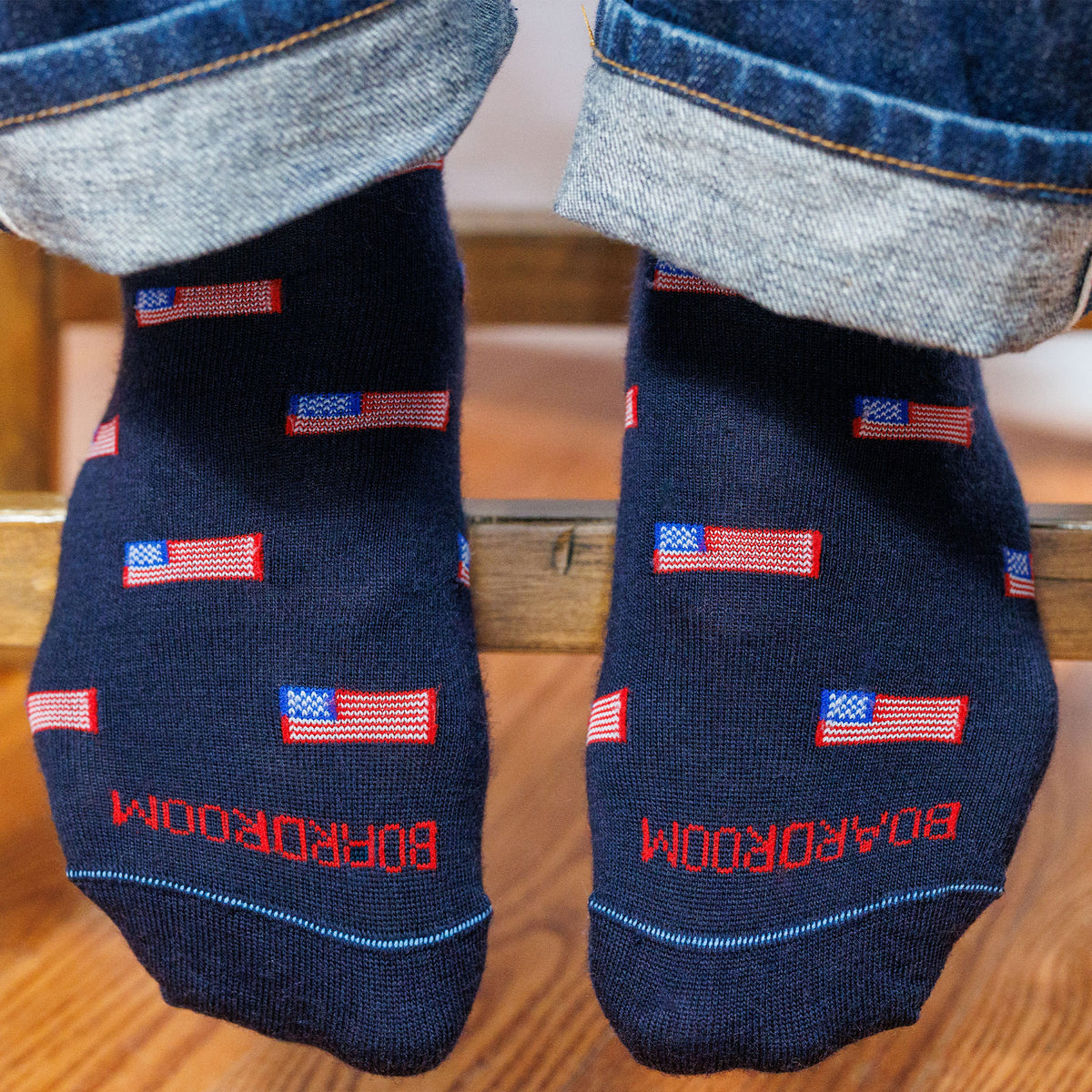man sitting on a stool wearing jeans and american flag patterned merino wool dress socks